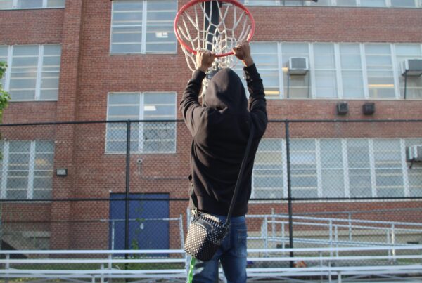 image of a boy on the basketball court handing from a basket ball rim.