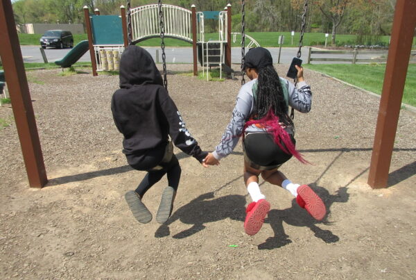 Image of two teenage girls at the playground holding hands on the swing.